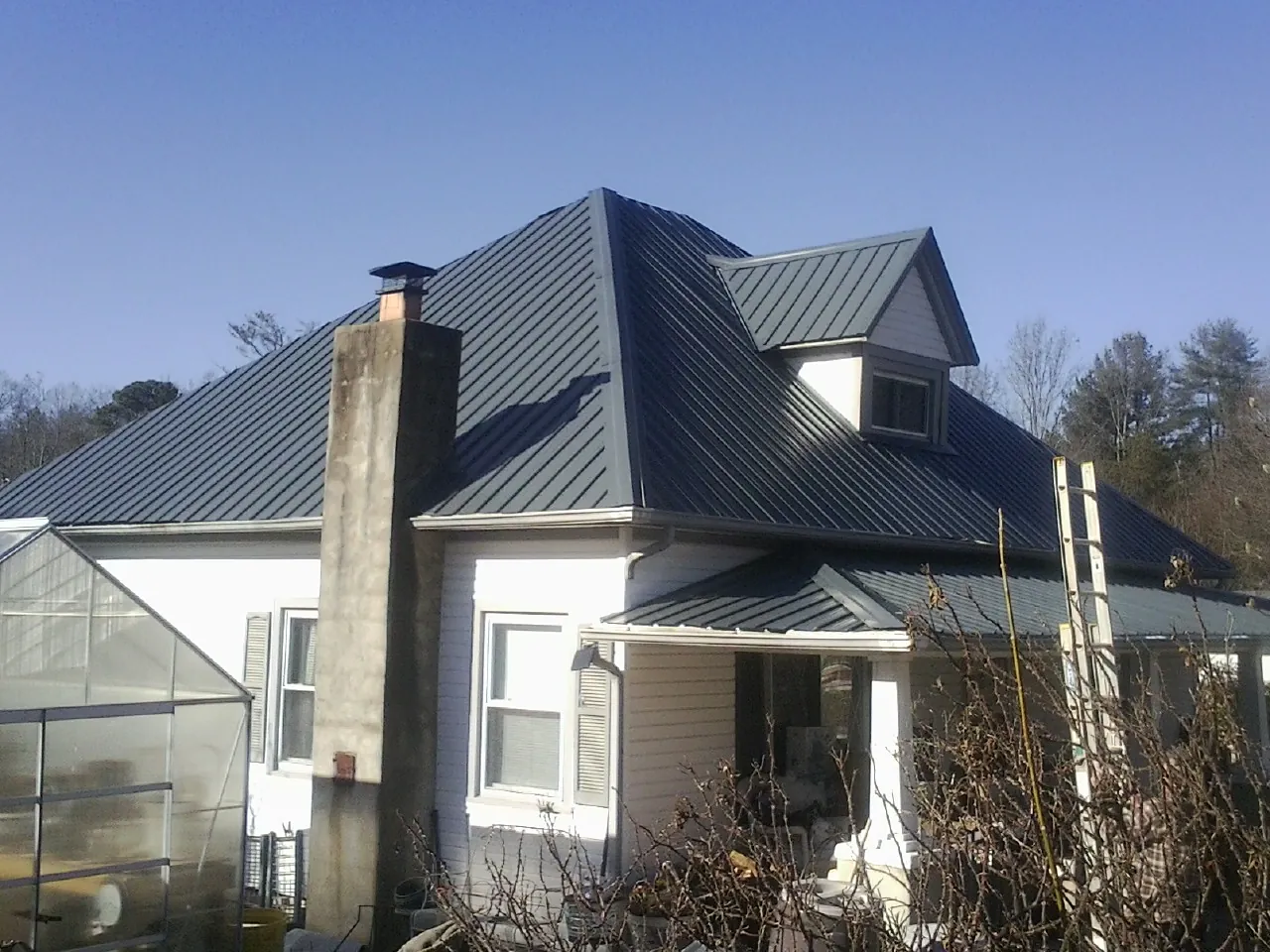 Dark blue standing seam metal roof on a white farmhouse with dormer — Slate & Tile Roof Repair by Roofing Brothers in Nemacolin