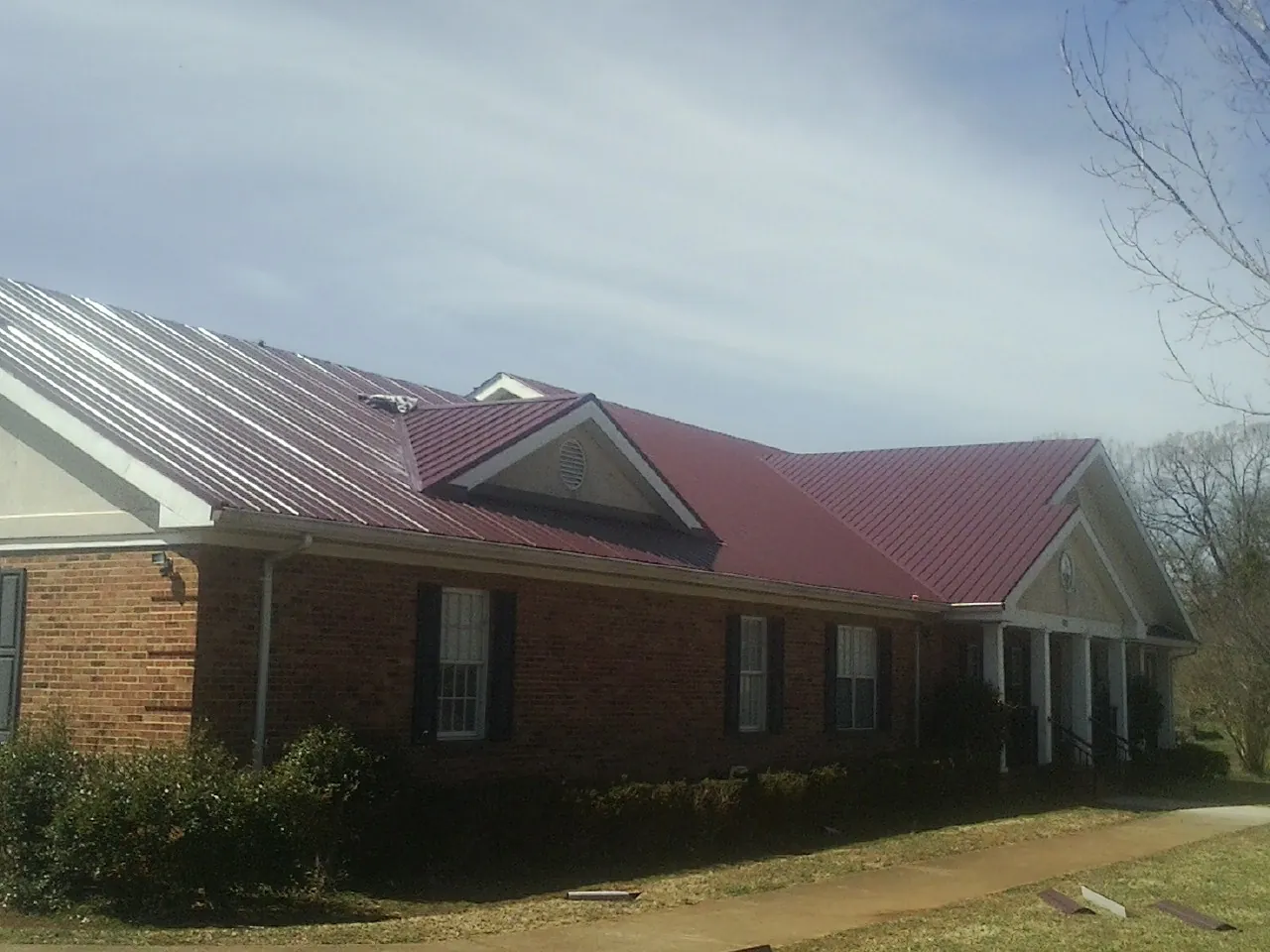 Red metal roof with gabled entries on a long brick building, from a Hail Damage Roof Repair job in Nemacolin