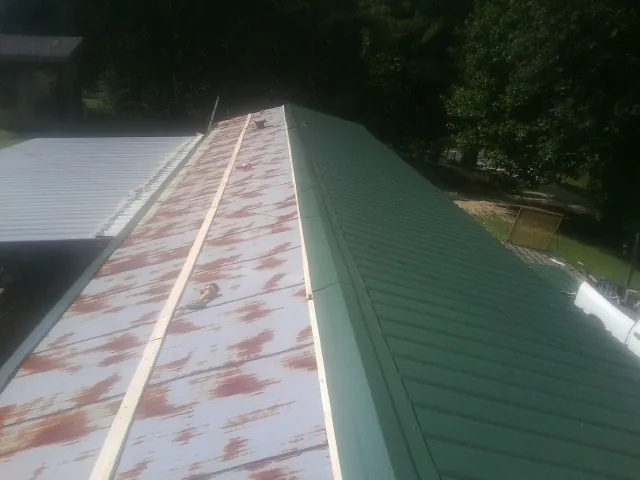 Old rusted panels beside newly installed green metal roofing — Wind Damage Roof Repair by Roofing Brothers in Nemacolin