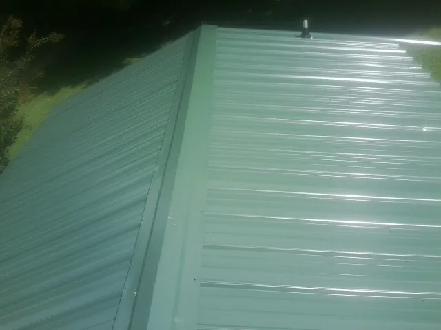New green metal panels meeting at the ridge of a roof — Flat Roof Repair work by our crew in Nemacolin