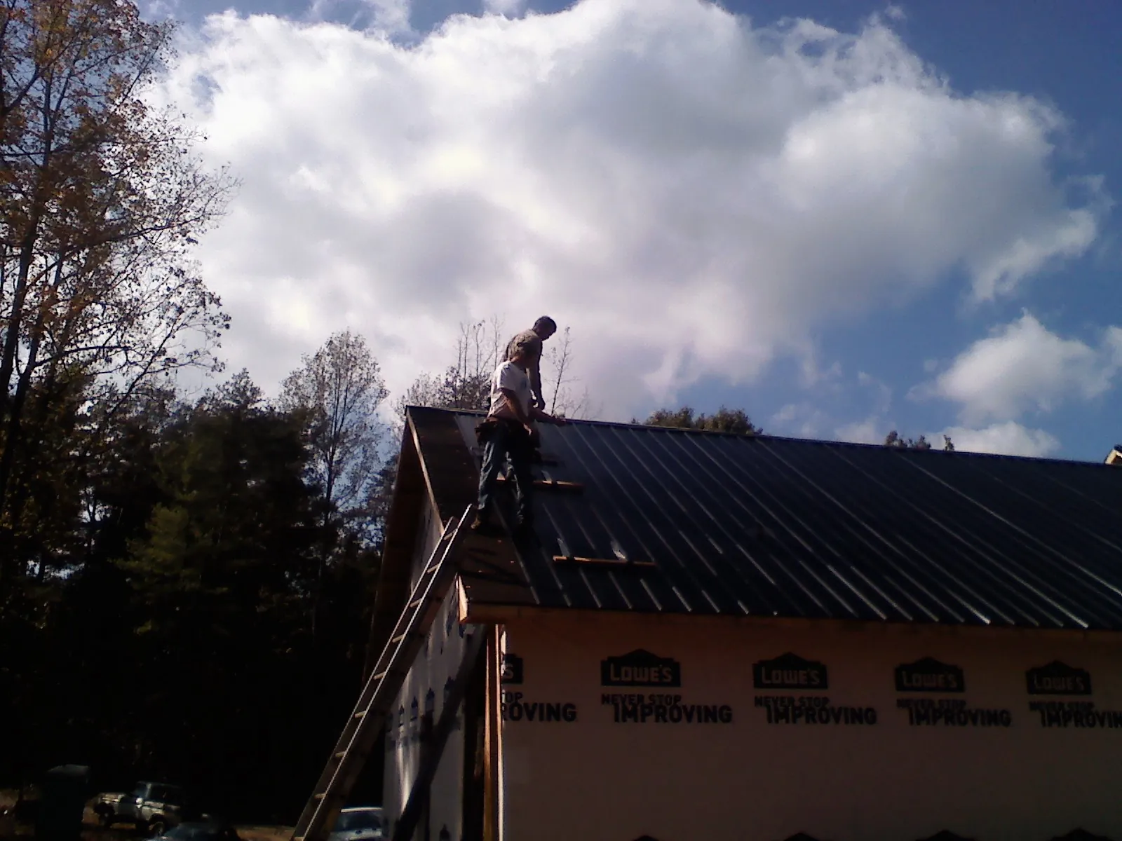 Roofer fastening dark metal panels high against a cloudy sky, from a Roof Inspection job in Nemacolin
