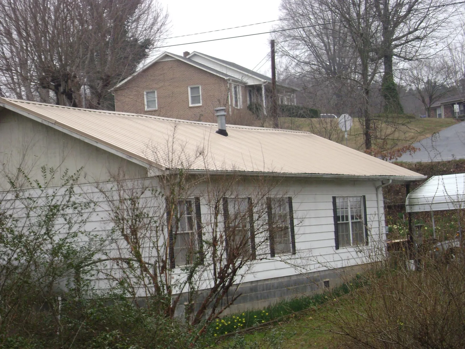 Tan metal roof on a white sided house set into a hillside — Commercial Roofing by Roofing Brothers in Nemacolin