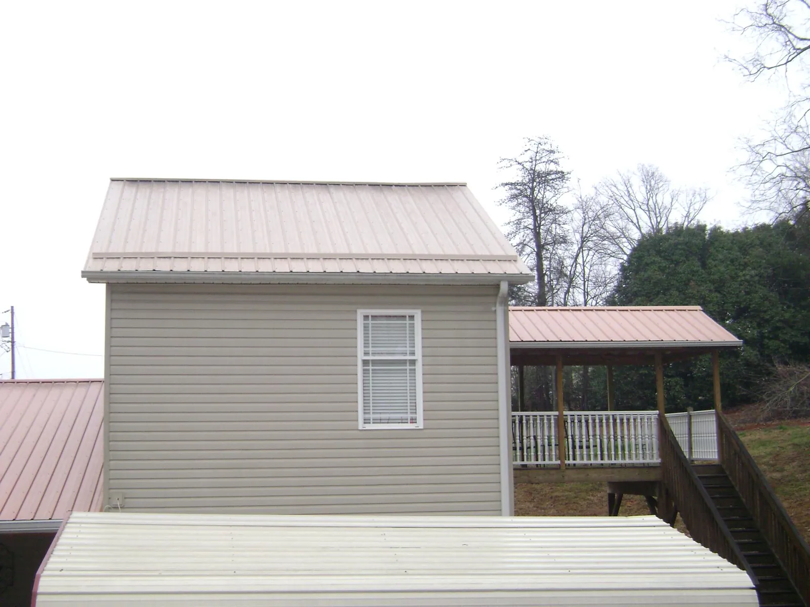 Tan metal roofs on a two story addition and attached porch, from a Roof Replacement job in Nemacolin